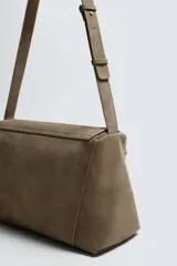 Bandolera de piel con acabado en serraje, diseño rectangular con solapa frontal y cierre magnético. Cuenta con un asa larga ajustable y compartimento interior con cierre de cremallera.
