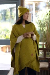 Ruana tejida color verde pistacho con flecos en el borde inferior y parche de cuero en la parte inferior.