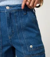 Short mom de tiro alto confeccionado en denim de algodón, con diseño de bolsillos tipo carpintero en el frente y bolsillos traseros. Presenta trabillas en la cintura y cierre tradicional.
