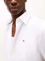 Camisa de manga corta blanca de Tommy Hilfiger confeccionada con popelín elástico de algodón BCI, con cuello abotonado, cierre con botones, detalles distintivos de Tommy Hilfiger y logo de Tommy Hilfiger bordado en el pecho.