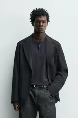 Blazer relaxed fit de estructura color gris, confeccionado en tejido con algodón, cuello con solapas de muesca, manga larga con botones en los puños y bolsillos de plastrón en la cadera.