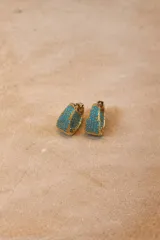 Aros tipo argolla con base metálica dorada e incrustaciones de cristales negros en toda su superficie frontal.