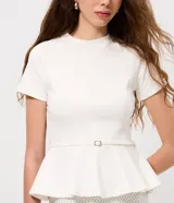 Blusa de punto Roma color celeste, con cuello alto, mangas cortas y diseño peplum. Presenta recortes estructurales y un cinturón integrado con hebilla metálica en la cintura, finalizando en un ruedo con volados.