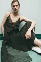 Top estampado con diseño geométrico en tonos verdes y marrones, confeccionado en viscosa 100%. Presenta escote en pico, tirantes finos y detalle de encaje negro a contraste. El bajo tiene un acabado asimétrico.