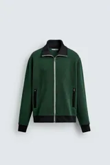Chaqueta regular fit color verde oscuro con detalles en negro en el cuello subido, los puños, el dobladillo inferior y los ribetes de los bolsillos. Cuenta con cierre frontal de cremallera metálica y bolsillos con cierre en la cadera.