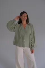 Blusa de color verde agua, con cuello en V, cierre frontal con botones y mangas largas abullonadas con puños elásticos. Presenta detalles bordados sutiles en la parte frontal y en las mangas.