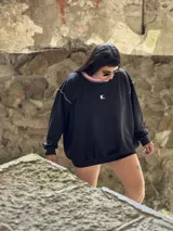 Buzo deportivo de verano (sin felpa) color negro, corte oversize, con cuello redondo y pespuntes contrastantes en color rosa pálido. Presenta una pequeña letra 'K.' bordada en el pecho.