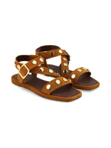 Sandalia plana de cuero gamuza en color camel, con tiras decoradas con tachas metálicas doradas y hebilla metálica de ajuste lateral.