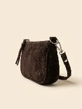 Cartera pequeña tipo bandolera confeccionada en gamuza color marrón oscuro, con cierre superior metálico y correa ajustable con herrajes plateados. Presenta un detalle de logo grabado en la parte inferior.