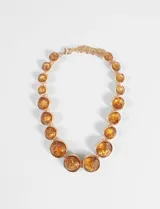 Collar tipo gargantilla con piedras circulares de acrílico en tono ámbar engarzadas en metal dorado, con cadena de extensión ajustable.