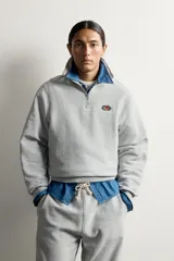 Sudadera gris de corte relaxed fit con cuello alto y cierre frontal de cremallera corta, confeccionada en algodón con interior de rizo afelpado. Presenta mangas largas, puños y bajo de rib, y un parche bordado con el logotipo de Fruit of the Loom en el pecho. Colección especial Fruit of the Loom x Zara.