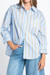 Camisa de corte oversize con estampado de rayas verticales en tonos azul y beige. Presenta cuello camisero clásico, cierre frontal con botones, bolsillo en el pecho y mangas largas con puños rectos.