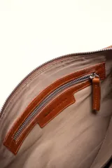 Cartera bandolera de cuero marrón con forma relajada, diseño de costuras curvas y detalles de nudos hechos a mano en las asas.