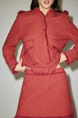 Chaqueta corta de tweed en color rojo, con cuello solapa, manga larga y bolsillos frontales con solapa. Presenta detalles deshilachados en los bordes y cierre frontal con cremallera oculta.
