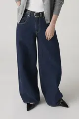 Jean de corte baggy y silueta barrel, confeccionado en denim rígido de color azul oscuro. Presenta costuras laterales curvadas que definen su forma característica, tiro alto y cierre frontal con botón y cremallera.