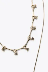 Pack de dos collares en tono dorado envejecido. El primero es un collar corto con eslabones de diseño orgánico y detalles de pequeñas esferas. El segundo es un collar largo de cadena fina con un dije central en forma de gota con una piedra marrón incrustada y borde labrado.