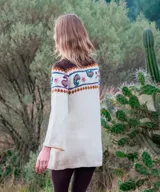 Vestido midi de punto color marfil, confeccionado artesanalmente en lana merino, con silueta en A, mangas largas oxford y cuello a la base. Presenta un diseño de bloques de color con bordados hechos a mano con motivos paisley y florales en tonos marrones, azules y rosados en la parte superior y las mangas.