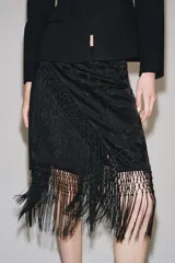 Falda corta de tiro medio, color negro, con diseño cruzado estilo pareo ajustable con lazada lateral. Cuenta con bordados tonales de motivos florales y bajo acabado con flecos largos.
