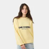 Suéter de punto grueso color amarillo, con corte cuadrado y ligeramente corto. Presenta cuello redondo, mangas largas con puños ajustados y el logo de la marca Eme Studios junto a la frase 'curated by ben ice' en jacquard oscuro en el centro del pecho.