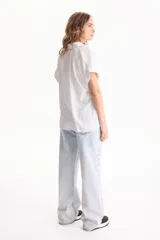 Camisa de viscosa con patrón de rayas verticales en tonos beige y blanco, cuello camisero, manga corta y cierre frontal con botones.