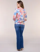 Blusa estampada Zac & Rachel con diseño floral en tonos rosados, azules y amarillos sobre base blanca. Presenta escote en V con botones frontales, mangas tres cuartos con presilla para arremangar y detalle de nudo en el ruedo.