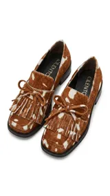 Mocasín de cuero con estampado animal print tipo vaca, de horma cuadrada. Presenta detalle de flecos y lazo decorativo en el empeine, con taco bajo cuadrado.