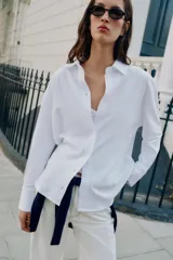 Camisa blanca de algodón con cuello solapa, manga larga y cierre frontal de botones.
