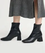 Bota de caña corta color negro, confeccionada en material sintético, con taco mediano bloque y puntera cuadrada.
