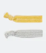 Set de dos gomitas de pelo, una dorada y otra plateada, con efecto metálico y nudo decorativo.