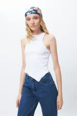 Top de algodón blanco sin mangas con cuello halter y bajo asimétrico en punta diagonal. Presenta un tejido de punto acanalado y un diseño inspirado en la estética de los años 2000.