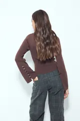 Top de punto acanalado color marrón, de manga larga y calce ajustado al cuerpo. Presenta escote redondo y detalle de botones en los puños.