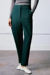 Pantalón de tiro alto confeccionado en mezcla de algodón, con diseño de volumen y costuras torcidas. Presenta bolsillos laterales y cierre frontal con cremallera, botón interior y ganchos metálicos ocultos.