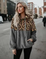 Buzo tipo canguro de polar con capucha y cierre frontal parcial. Presenta un diseño combinado con estampado animal print de leopardo en la parte superior y color gris liso en la parte inferior y mangas. Cuenta con bolsillo frontal tipo canguro y puños elásticos.