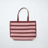 Bolso tipo tote grande de diseño estructurado, con patrón de rayas horizontales en tonos bordó y rosado, y doble asa superior de hombro.