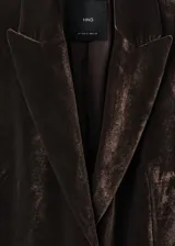 Blazer de corte recto confeccionado en tejido de terciopelo color marrón oscuro. Presenta cuello con solapas de muesca, cierre frontal con un botón, mangas largas con puños abotonados y dos bolsillos laterales con solapa. Incluye forro interior.