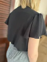 Blusa color blanco roto, confeccionada en crepé, con escote en V, nudo frontal y mangas cortas amplias con volados.