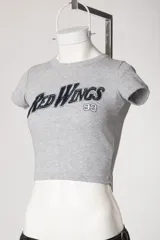 Remera tipo baby tee blanca de manga corta, con cuello redondo y diseño ajustado al cuerpo con estampado y bordado frontal "Red Wings 93".