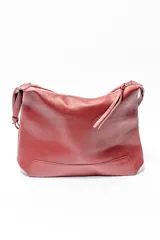 Bolso de hombro tipo hobo en color rojo oscuro, confeccionado en cuero con textura granulada. Presenta un diseño minimalista con cierre superior de cremallera y tirador largo.