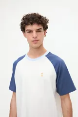 Remera estilo raglán color blanco en el cuerpo con mangas cortas color arena y cuello redondo marrón. Presenta un pequeño bordado en el pecho.