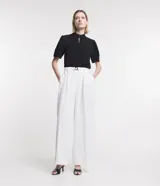 Pantalón de corte amplio tipo pantalona, confeccionado en tejido plano de poliéster. Presenta cintura alta con cinturón elástico integrado que incluye hebilla metálica, pliegues frontales y bolsillos laterales.