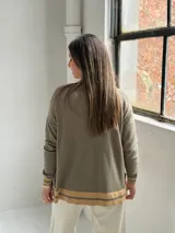 Sweater de punto en color verde oliva, con cuello en V y diseño holgado. Presenta detalles de franjas en color beige en el cuello, los puños y el ruedo.