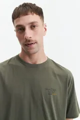 Remera de manga corta color gris claro, con cuello redondo y estampado pequeño en el pecho con texto en rojo y negro.