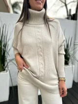 Polerón de punto color beige con cuello alto, diseño holgado y detalle de trenzado vertical en el frente.