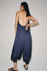 Mono largo satinado de color azul marino, con cuello halter, escote en V profundo y espalda descubierta. Presenta diseño plisado y bajo abullonado con terminación en puño.