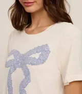 Blusa de pijama de viscosa color crema, con cuello redondo, mangas cortas y estampado frontal de un lazo grande en color azul.