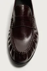 Mocasín de vestir negro de estilo clásico con detalle de antifaz en la parte superior, suela a tono y ligero tacón.