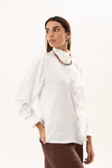 Camisa blanca de cuello alto con volados frontales a lo largo de la botonadura, manga larga con puños con volados y cierre frontal con botones.