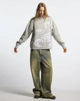 Suéter de punto color gris claro con diseño de escorpión en color blanco tejido en el frente. Presenta cuello redondo, puños y cintura con terminaciones acanaladas, y un corte holgado tipo boxy fit.