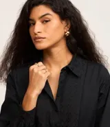 Vestido corto de corte evasé confeccionado en tricolina de algodón, color azul. Presenta cuello camisero, cierre frontal de botones y un panel central con detalle bordado calado. Posee mangas largas con puños abotonados.