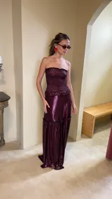Vestido largo strapless de lamé elastizado color bordó, con cuerpo fruncido tipo corsel y falda larga amplia con volados y frunces.